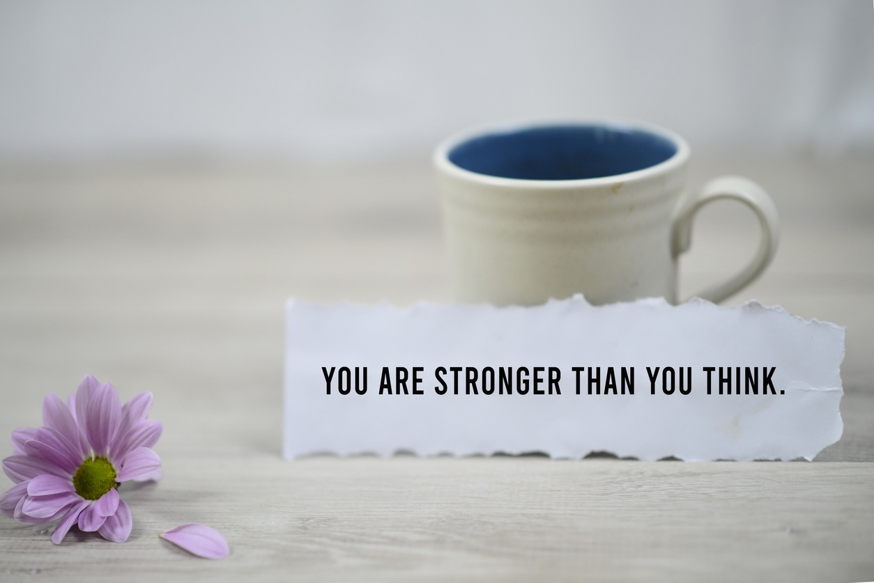 Inspirational quote - You are stronger than you think. With a cup of morning coffee and beautiful purple daisy flower on white wooden table background. Motivation words on paper note with motivating text concept.