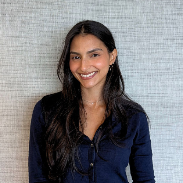 Portrait of a smiling woman with long dark hair in a navy blue button-down shirt against a light textured wall.
